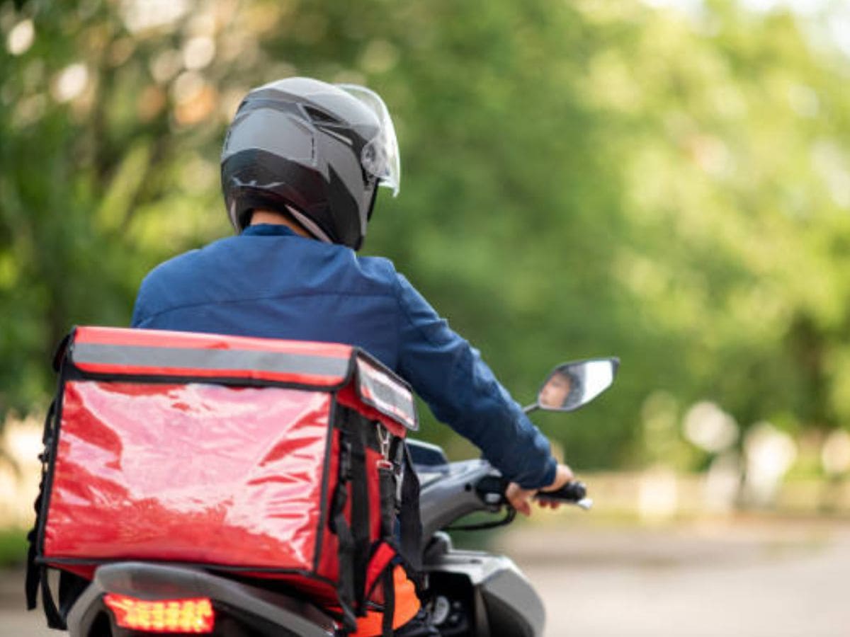 Entregador de moto usando capacete e colete refletivo dirigindo com atenção ao trânsito urbano