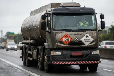 Caminhão-tanque com placas de sinalização de perigo sendo conduzido por motorista de transporte de inflamáveis.